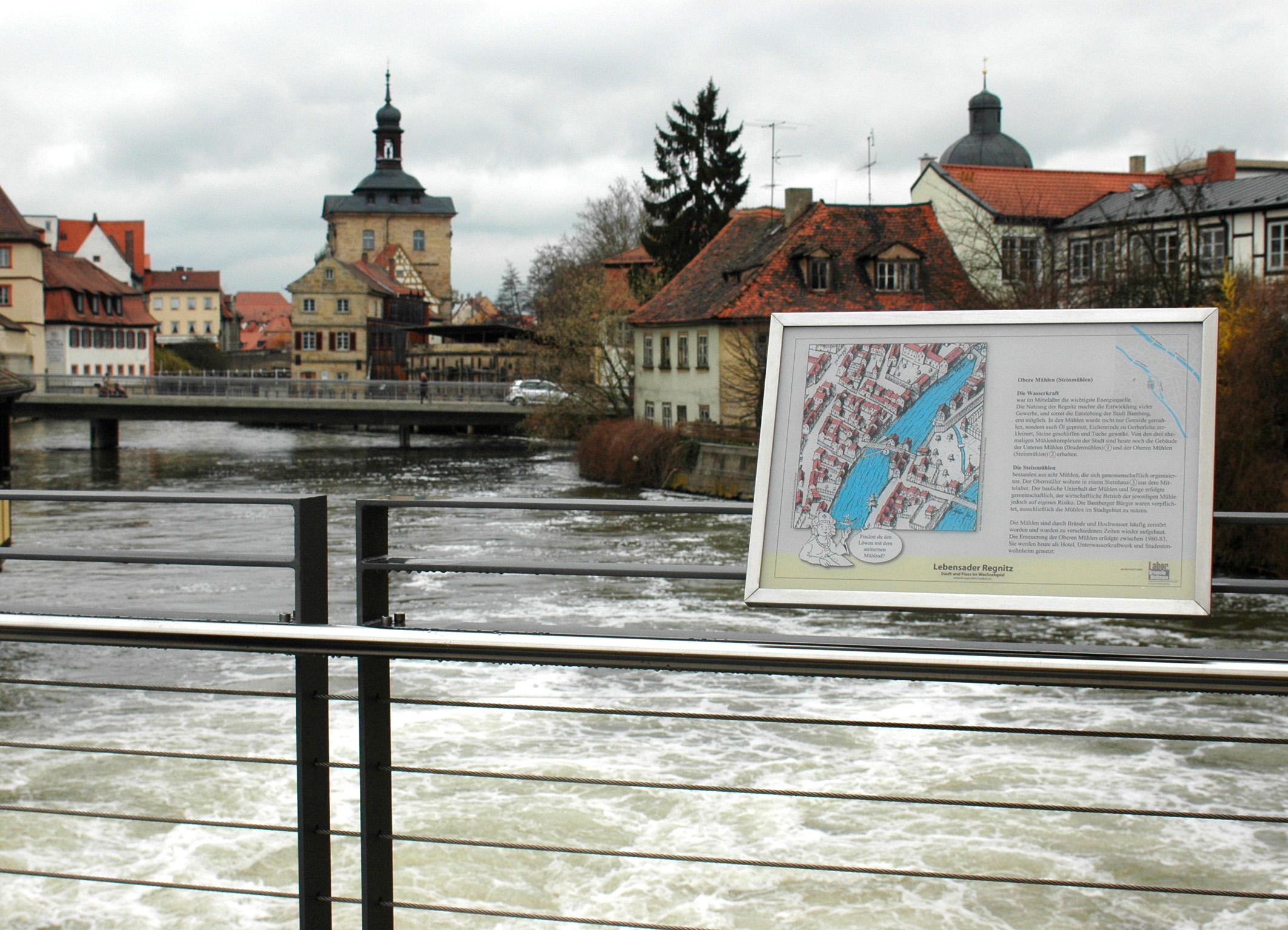 Flusspfadtafel Obere Mühlen in Bamberg mit Blick über die Regnitz auf die Unteren Mühlen und das Alte Rathaus. Foto: Christine Schmitt