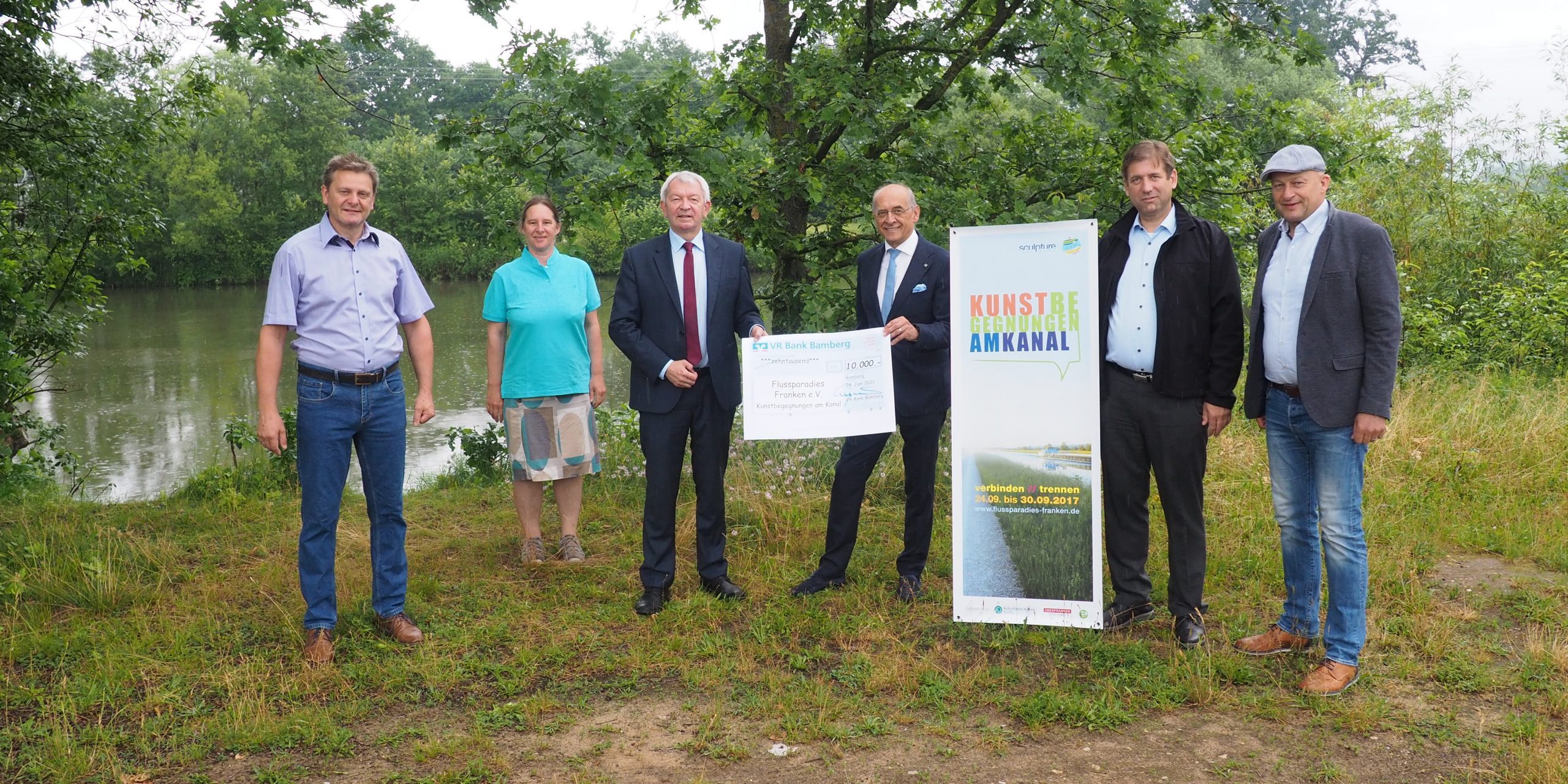 Ganz konkret verbindet das Projekt „Kunstbegegnungen am Kanal verbinden//trennen“ die Landkreise Bamberg und Forchheim. Darum wurde für die Übergabe des Spendenschecks in Höhe von 10.000,- Euro als symbolischer Ort die Landkreisgrenze gewählt, die zwischen der Gemeinde Altendorf und dem Markt Eggolsheim verläuft. V.l.n.r: Bürgermeister Karl-Heinz Wagner (Gemeinde Altendorf), Anne Schmitt (Geschäftsführerin Flussparadies Franken e. V.), Landrat Johann Kalb (Lkr. Bamberg), Vorstandsvorsitzender