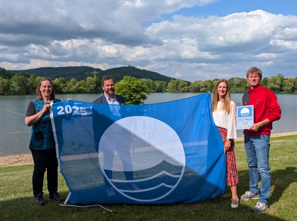 Zum 15. Mal ausgezeichnet Ostsee Bad Staffelstein. v.l.n.r.: Anne Schmitt Geschäftsführerin Flussparadies Franken, Bürgermeister Mario Schönwald, Tourismusleiterin Anne Schneider und Martin Lüders (Geschäftsführer Freizeit GmbH) präsentieren die Blaue Flagge am Ostsee Bad Staffelstein. Foto: Kur & Tourismus Service Bad Staffelstein / Ina Hennemann
