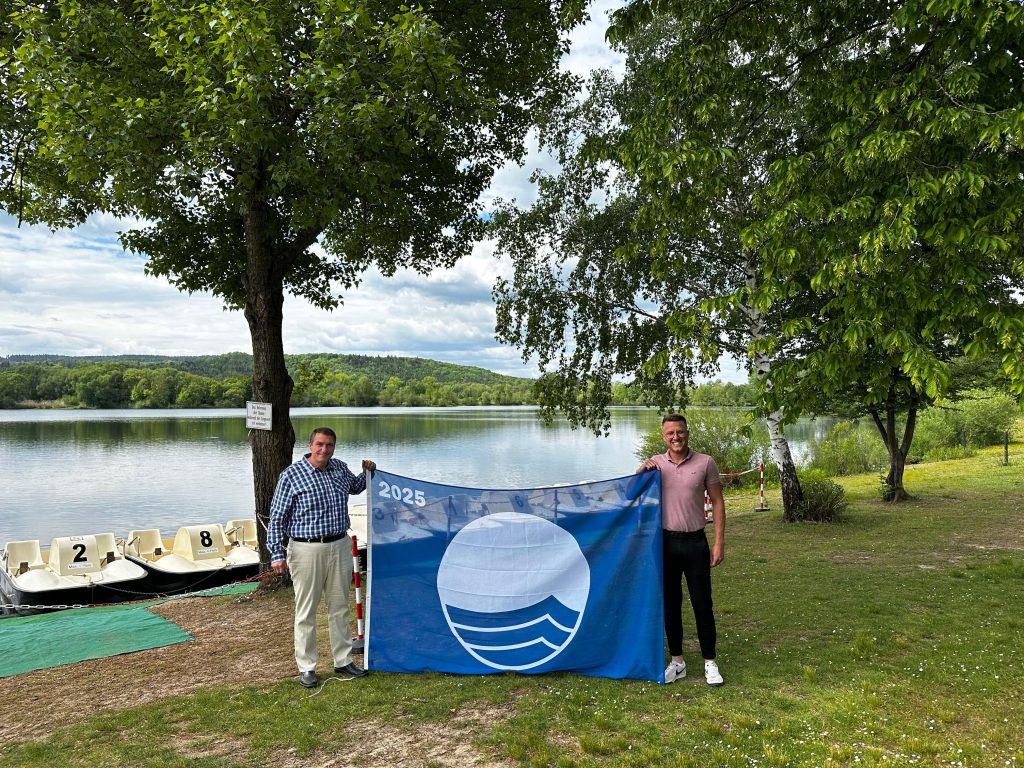 Zum 11. Mal ausgezeichnet Rudufersee. v.l.n.r.: Bürgermeister Jochen Weber und Seenbeauftragter Yannic Wildner präsentieren die Blaue Flagge am Rudufersee Michelau i.OFr. Foto: Gemeinde Michelau i. OFr.