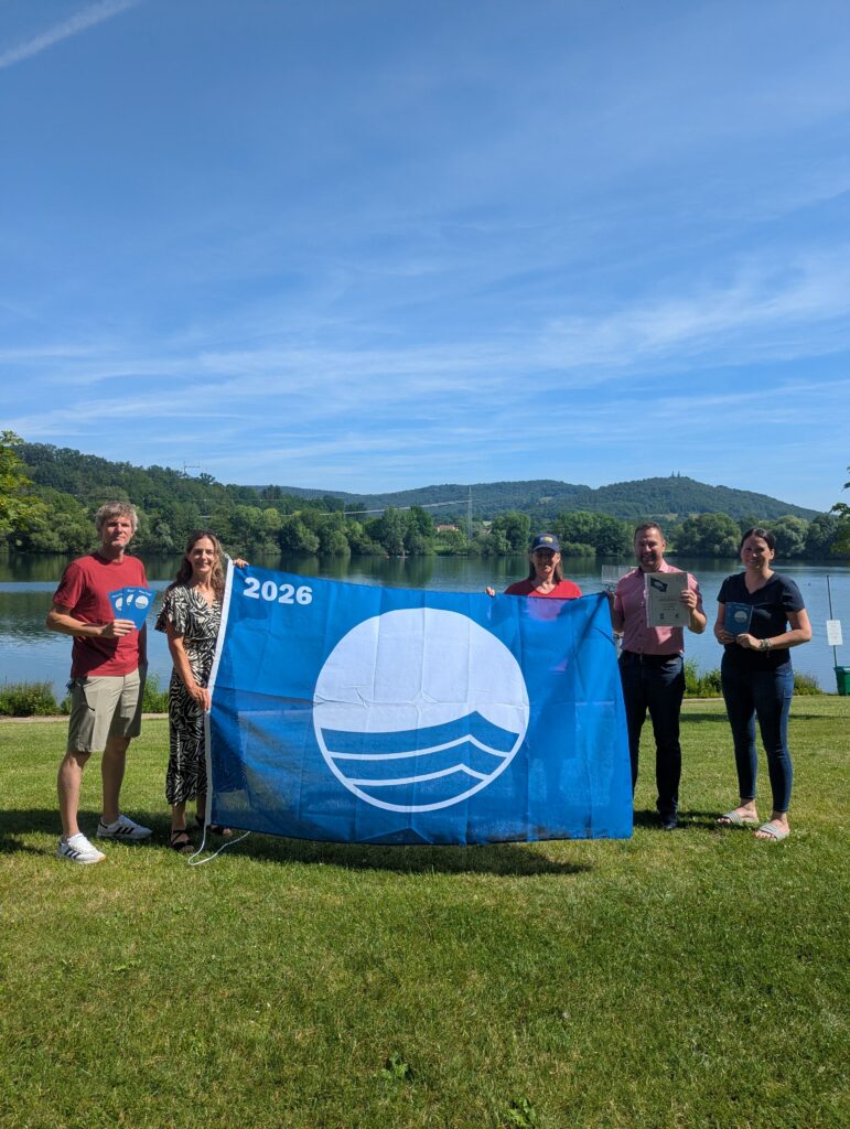 Gemeinsames Hissen der Flagge am Ostsee Bad Staffelstein (von links): Martin Lüders (Freizeit GmbH), Anne Maria Schneider (Leitung Tourist Information Bad Staffelstein), Anne Schmitt (Flussparadies Franken), Mario Schönwald (Erster Bürgermeister Stadt Bad Staffelstein), Susanne Müller (Freizeit GmbH). Foto: Tourist Information Bad Staffelstein / Carolin Böhmer