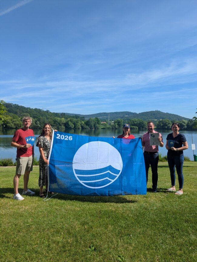 Gemeinsames Hissen der Flagge am Ostsee Bad Staffelstein (von links): Martin Lüders (Freizeit GmbH), Anne Maria Schneider (Leitung Tourist Information Bad Staffelstein), Anne Schmitt (Flussparadies Franken), Mario Schönwald (Erster Bürgermeister Stadt Bad Staffelstein), Susanne Müller (Freizeit GmbH). Foto: Tourist Information Bad Staffelstein / Carolin Böhmer Gemeinsames Hissen der Flagge am Ostsee Bad Staffelstein (von links): Martin Lüders (Freizeit GmbH), Anne Maria Schneider (Leitung Tourist Information Bad Staffelstein), Anne Schmitt (Flussparadies Franken), Mario Schönwald (Erster Bürgermeister Stadt Bad Staffelstein), Susanne Müller (Freizeit GmbH). Foto: Tourist Information Bad Staffelstein / Carolin Böhmer